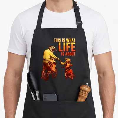 Tablier de cuisine noir avec illustration d'un père et fils en moto cross et le texte This Is What Life Is About.