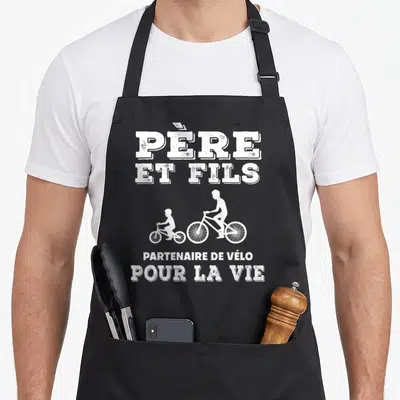Tablier de cuisine noir avec silhouettes de cyclistes et texte père et fils partenaire de vélo pour la vie en blanc.