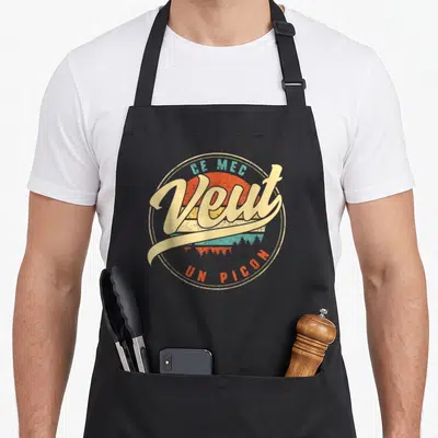 Tablier de cuisine noir avec logo circulaire vintage Ce Mec Veut Un Picon sur fond de soleil orange et turquoise.
