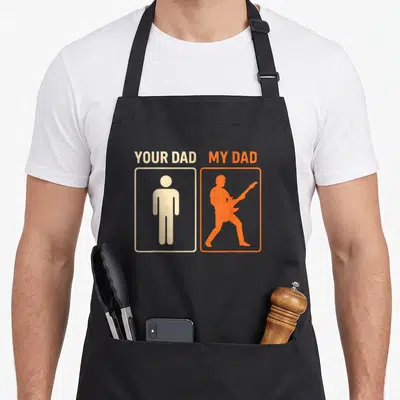 Tablier de cuisine noir avec silhouette orange rocker et texte Your Dad My Dad imprimé en haut.