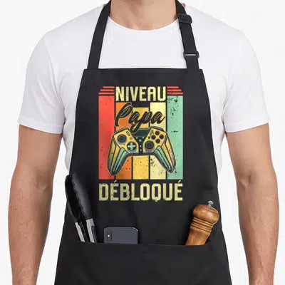 Tablier de cuisine noir avec illustration vintage manette de jeu et texte Niveau Papa Débloqué.