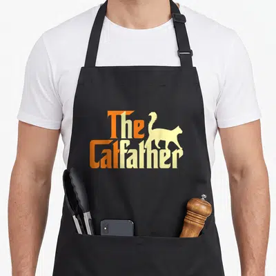 Tablier de cuisine noir avec le texte The Catfather et silhouette de chat orange et jaune.