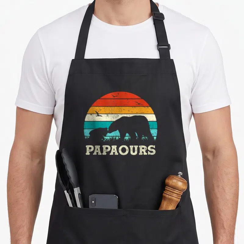 Tablier de cuisine noir avec silhouette d'ours et texte Papaours sur fond de soleil rayé rétro.