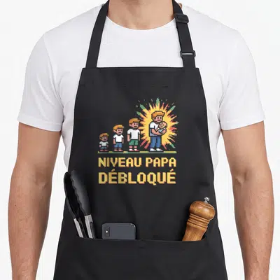 Tablier de cuisine noir avec illustration pixel art famille et texte Niveau Papa Débloqué en jaune.