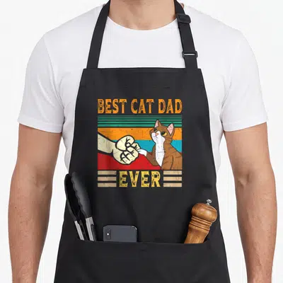 Tablier de cuisine noir avec illustration d'un chat et d'une main se faisant un poing sur fond rayé.