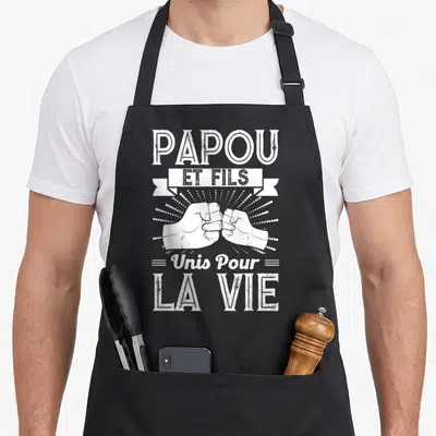 Tablier de cuisine noir avec illustration blanche de deux poings se touchant et le texte Papou et Fils Unis Pour La Vie.
