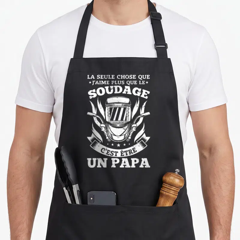 Tablier de cuisine noir avec illustration d'un casque de soudage et texte blanc sur fond uni.