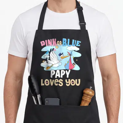 Tablier de cuisine noir avec illustration de cigogne transportant un bébé dans un drap rose ou bleu sous le texte Pink or Blue Papy Loves You.