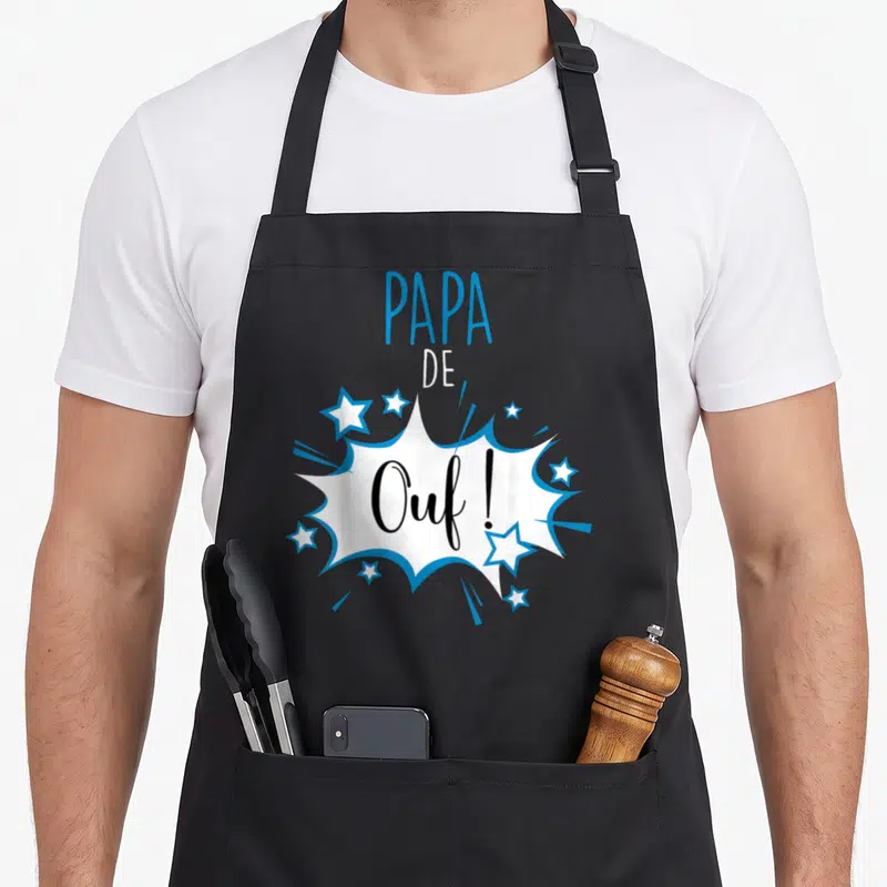 Tablier de cuisine noir avec motif Papa de Ouf en bulle de bande dessinée bleue et blanche entourée d'étoiles.