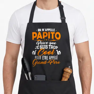 Tablier de cuisine noir avec l'inscription Papito très cool et deux pouces levés blancs sur fond gris uni.