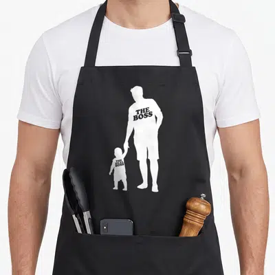 Tablier de cuisine noir avec silhouettes blanche père et enfant portant des inscriptions humoristiques sur le torse.