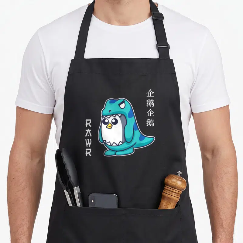 Tablier de cuisine noir avec un pingouin en costume de dinosaure vert et le mot Rawr imprimé sur le côté.