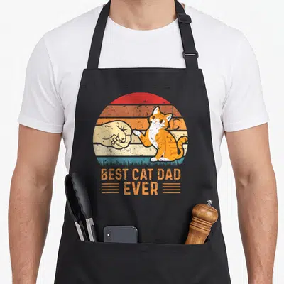 Tablier de cuisine noir avec illustration d'un chat tigré effectuant un poing contre une main humaine sur fond rétro.