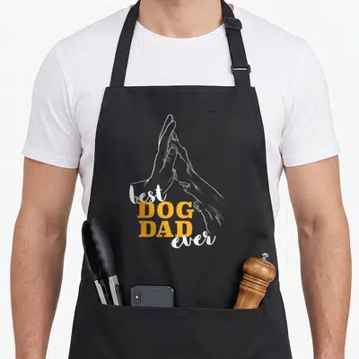 Tablier de cuisine noir avec illustration de mains jointes et texte best dog dad ever en orange et blanc.