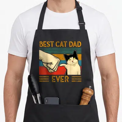 Tablier de cuisine noir avec illustration vintage d'un chat bicolore et d'une main en high five sur fond rayé coloré.