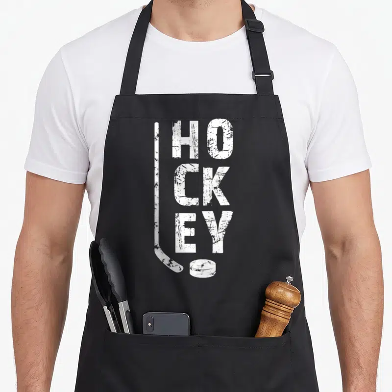 Tablier de cuisine noir avec inscription blanche HOCKEY verticale, bâton et palet en bas à droite.