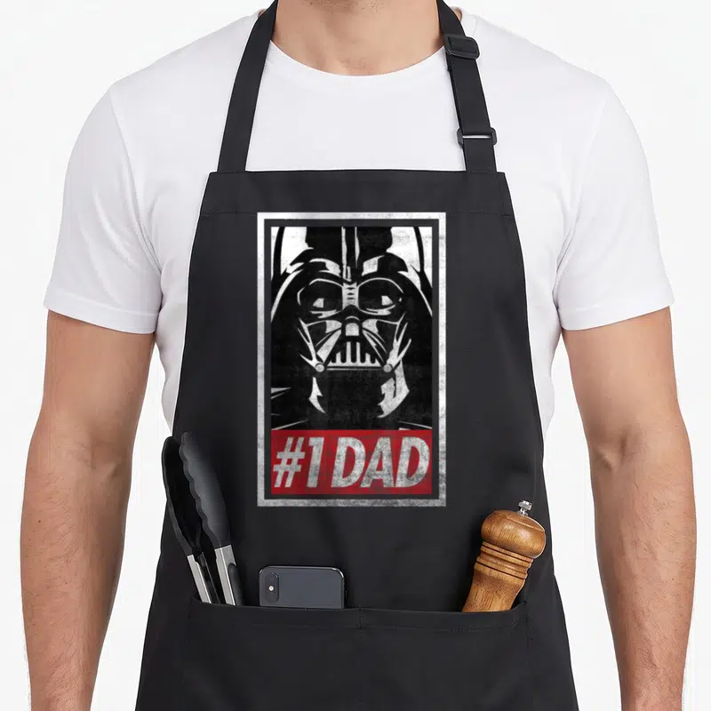 Tablier de cuisine noir avec portrait stylisé de Dark Vador et bande rouge portant l'inscription #1 DAD en blanc.