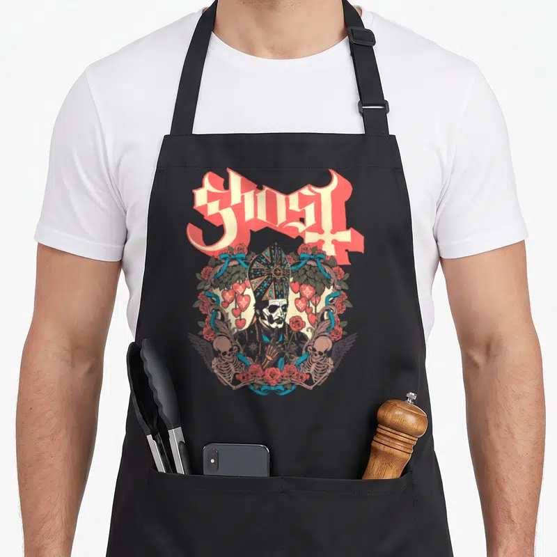 Tablier de cuisine noir avec illustration gothique d'un personnage en chapeau pontifical entouré de roses et de cœurs.