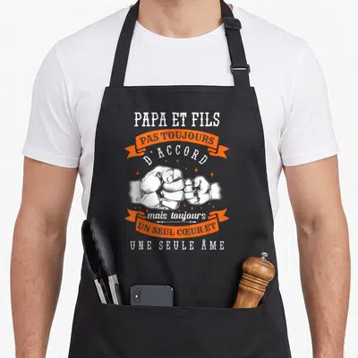 Tablier de cuisine noir avec poing se touchant et texte blanc orange sur fond uni.