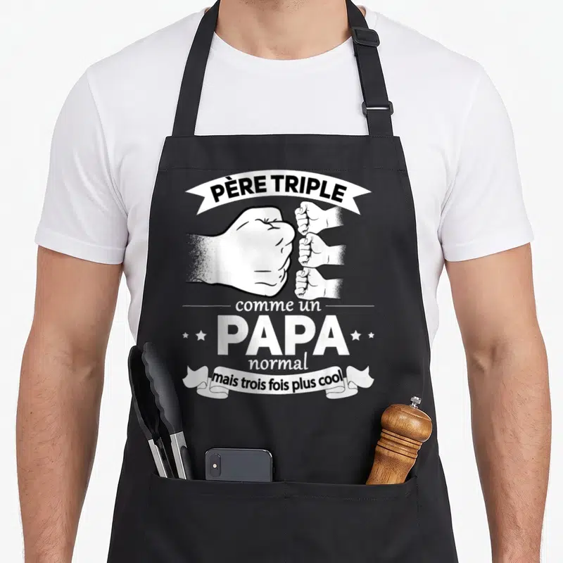 Tablier de cuisine noir avec illustration poings et texte Père triple comme un Papa normal mais trois fois plus cool en blanc.