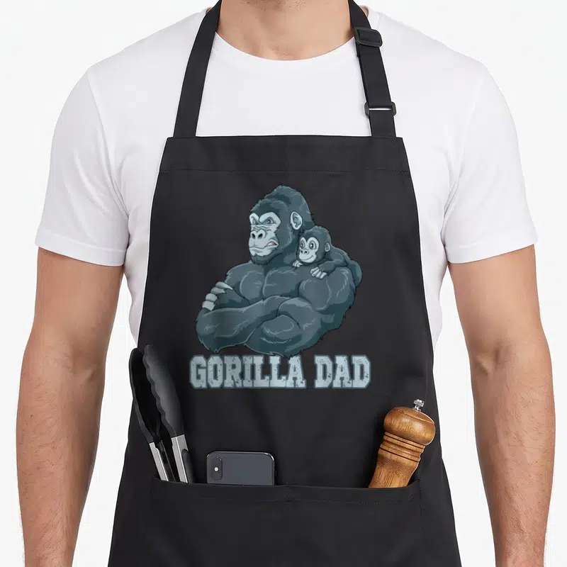Tablier de cuisine noir avec illustration d'un gorille musclé portant un bébé sur l'épaule et le texte GORILLA DAD.