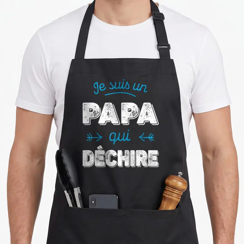 Tablier de cuisine noir avec le texte Je suis un Papa qui déchire en blanc et bleu.