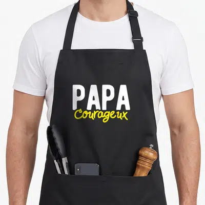 Tablier de cuisine noir avec l'inscription Papa Courageux en lettres blanches et jaunes stylisées au centre.