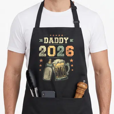 Tablier de cuisine noir avec illustration vintage Daddy 2026, biberon et grande bière sous des étoiles orange.