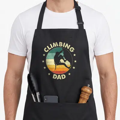 Tablier de cuisine noir avec illustration vintage Climbing Dad et silhouette d'escaladeur entourée d'étoiles.