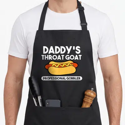 Tablier de cuisine noir avec illustration de hotdog et texte Daddy's Throat Goat en blanc.