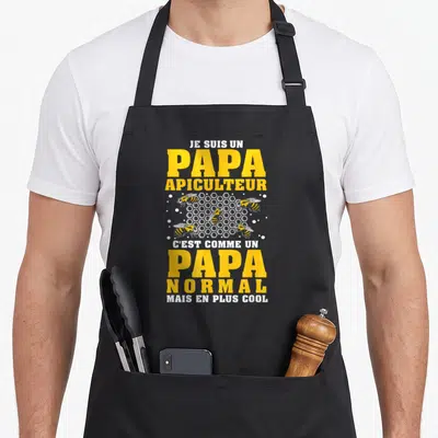 Tablier de cuisine noir avec inscription jaune et blanche Je suis un papa apiculteur illustré par des abeilles autour d'une ruche géométrique.