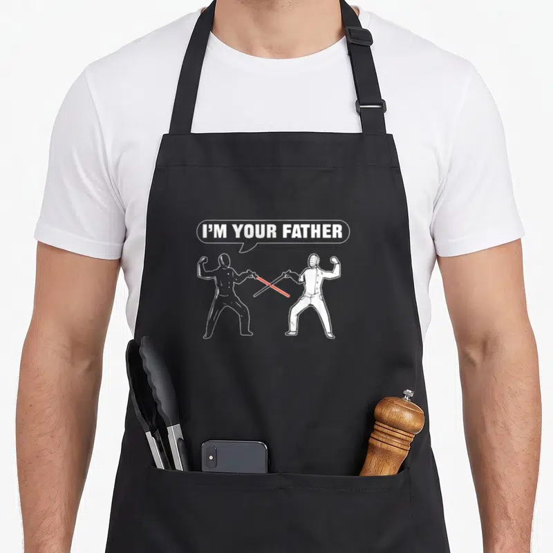 Tablier de cuisine noir avec deux silhouettes s'affrontant au sabre laser et une bulle de dialogue.