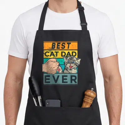Tablier de cuisine noir avec illustration Best Cat Dad Ever et poignée de main féline sur fond coloré.