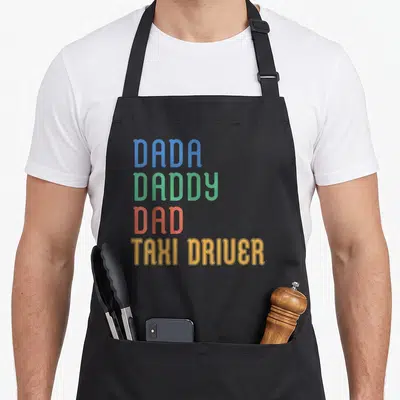 Tablier de cuisine noir avec les textes Dada Daddy Dad Taxi Driver imprimés en couleurs vives sur le devant.