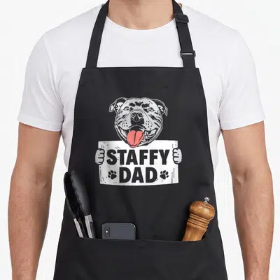Tablier de cuisine noir avec illustration d'un Staffordshire Bull Terrier tenant une pancarteStaffy Dad en gris et rouge.