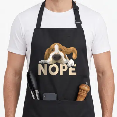 Tablier de cuisine noir avec illustration d'un basset hound posant ses pattes sur le mot NOPE en lettres capitales beige.