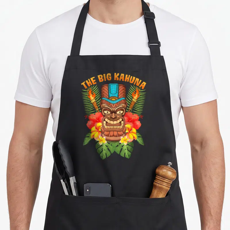 Tablier de cuisine noir avec illustration tiki The Big Kahuna, torches et fleurs tropicales.