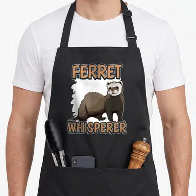 Tablier de cuisine noir avec illustration de furet et texte Ferret Whisperer en orange et noir.