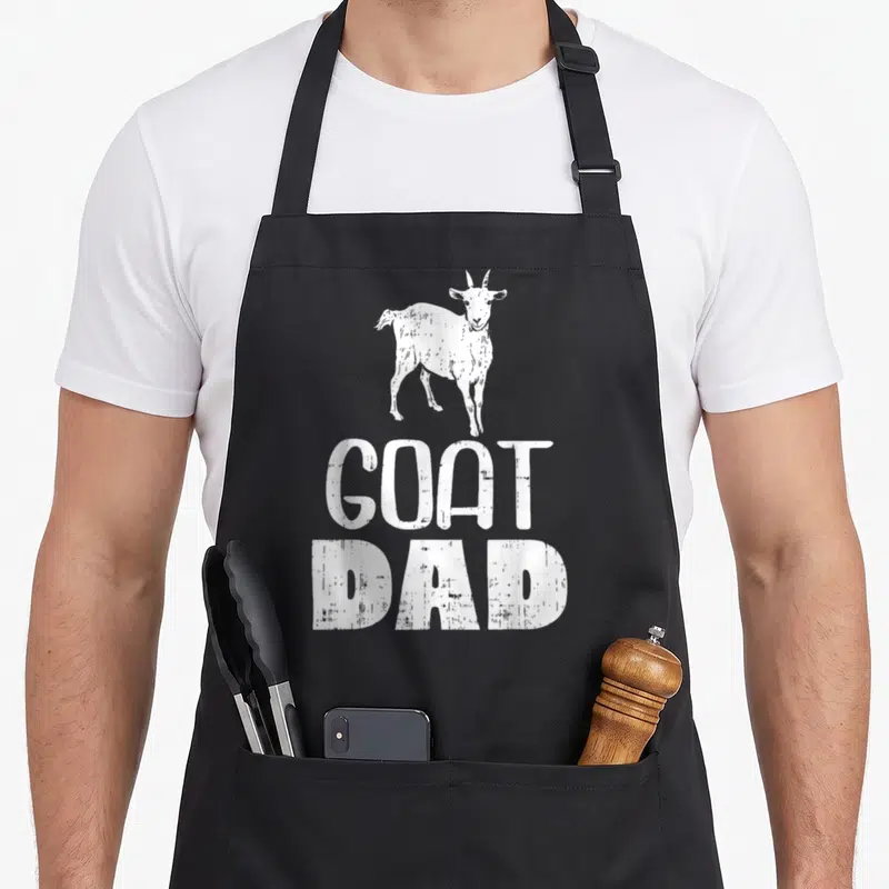 Tablier de cuisine noir avec une chèvre blanche et le texte Goat Dad en lettres capitales blanches texturées.