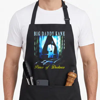 Tablier de cuisine noir avec illustration d'un homme en costume blanc sous des rideaux bleus et le texte Big Daddy Kane.