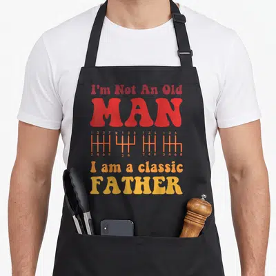 Tablier de cuisine noir avec inscription rouge et orange sur fond gris représentant un levier de vitesse.