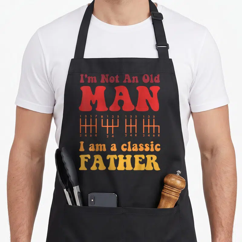 Tablier de cuisine noir avec inscription rouge et orange sur fond gris représentant un levier de vitesse.