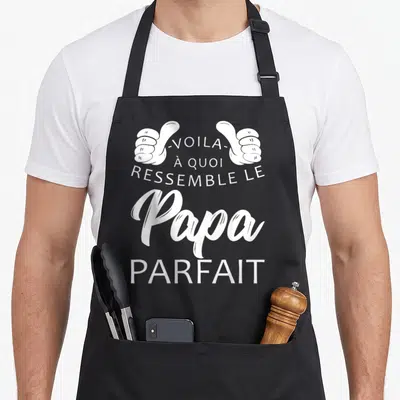 Tablier de cuisine noir avec inscription blanche Voila à quoi ressemble le Papa Parfait encadrée par deux pouces levés stylisés.