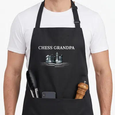 Tablier de cuisine noir avec l'inscription CHESS GRANDPA et des pièces d'échecs blanches et noires posées sur un damier.