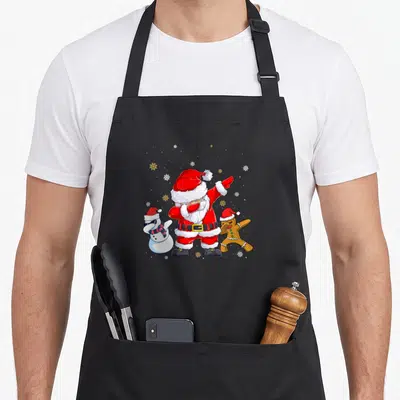 Tablier de cuisine noir avec illustration colorée d'un Père Noël faisant le dab entouré d'un snowman et d'un biscuit festif.