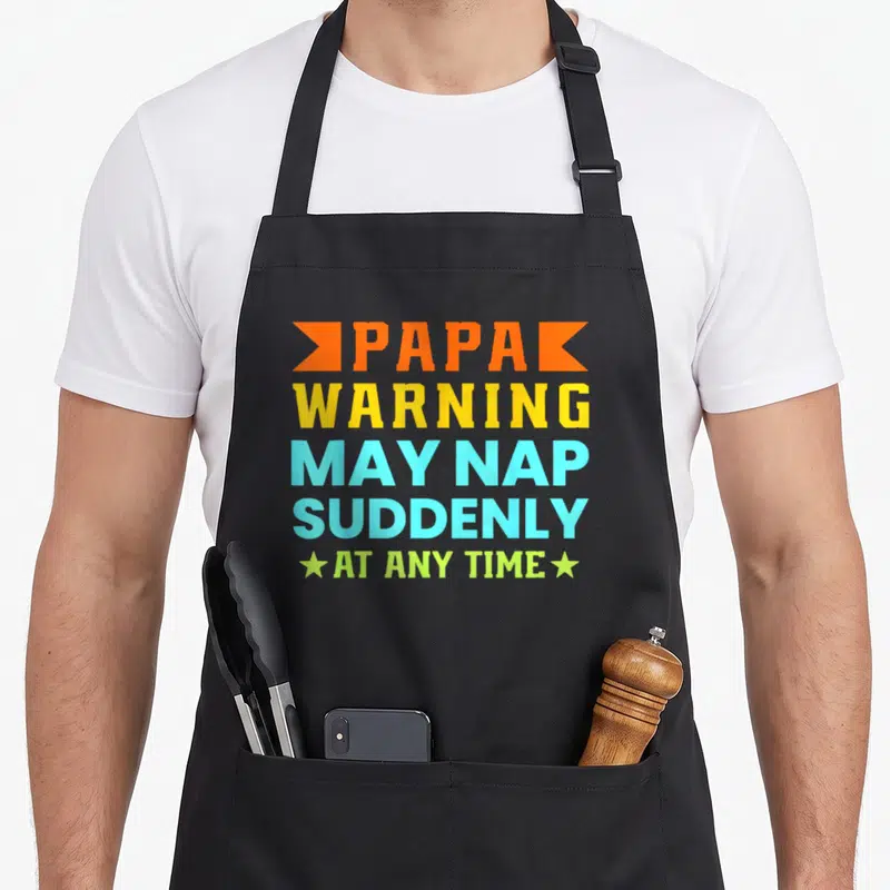 Tablier de cuisine noir avec un message multicolore sur le thème de la sieste du papa.