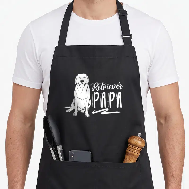 Tablier de cuisine noir avec illustration blanche d'un chien retriever assis et le texte Retriever PAPA.