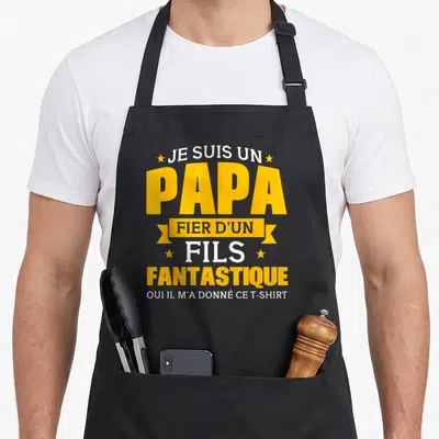 Tablier de cuisine noir avec texte jaune et blanc proclamant être un papa fier d'un fils fantastique.