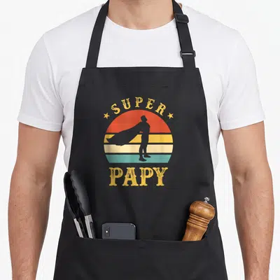 Tablier de cuisine noir avec silhouette super-héros et texte Super Papy Meilleur Grand-père du Monde en style vintage coloré.