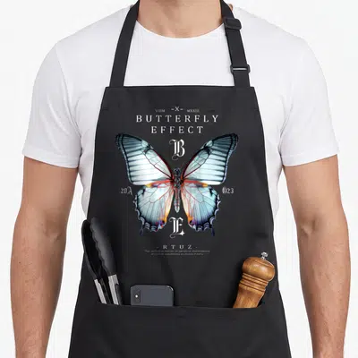 Tablier de cuisine noir avec un grand papillon détaillé et le texte Butterfly Effect en typographie blanche vintage.